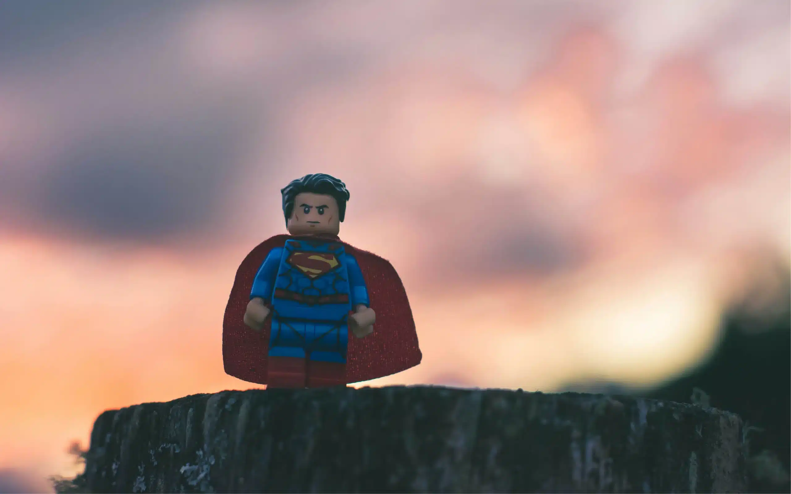 lego superman standing on log with colorful sky in background